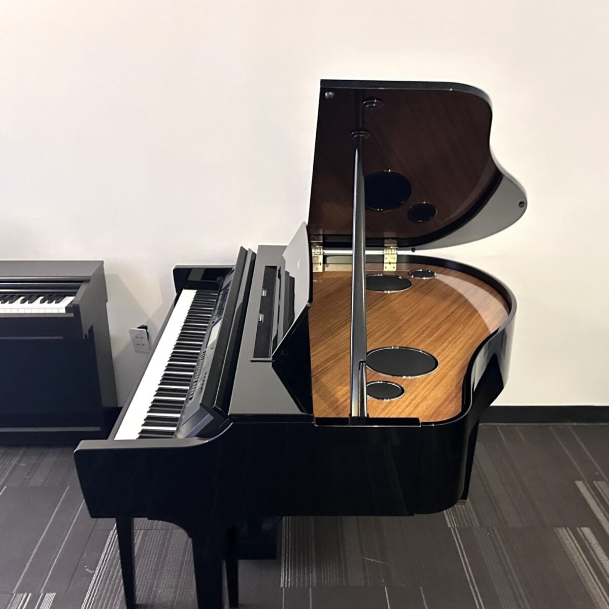 Black grand piano with open lid in a showroom setting.