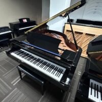 Black grand piano with open lid in showroom, featuring sleek finish and a polished keyboard.