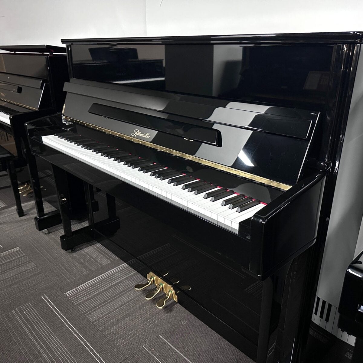 Upright Rippen piano with black gloss finish in a showroom setting.