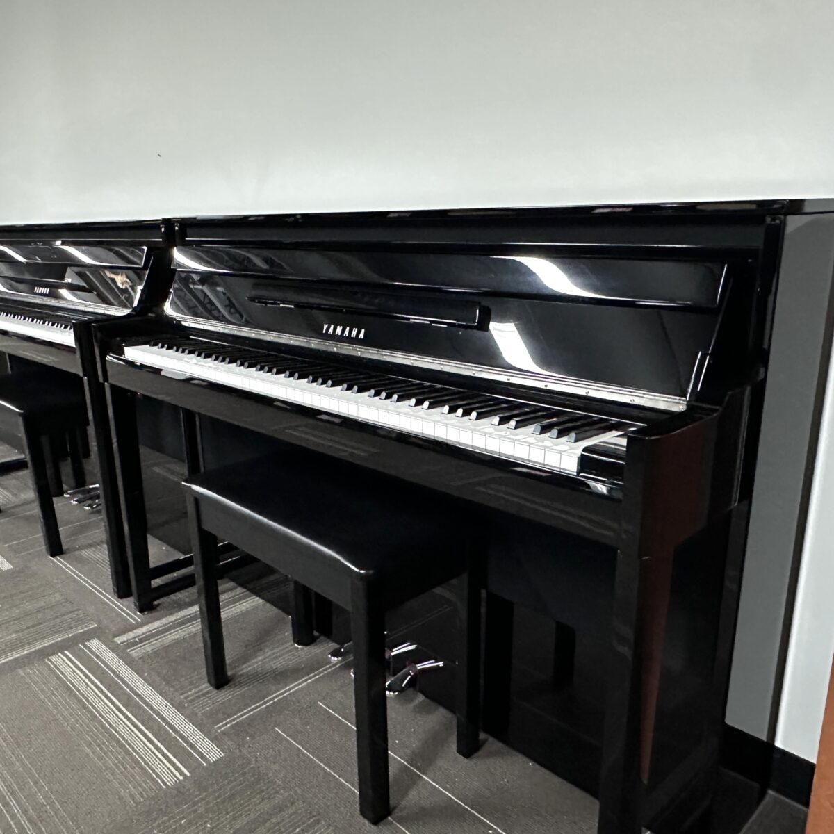 Yamaha upright pianos with black finish in a showroom setting with matching benches.