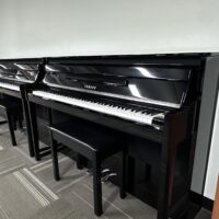 Yamaha upright pianos with black finish in a showroom setting with matching benches.