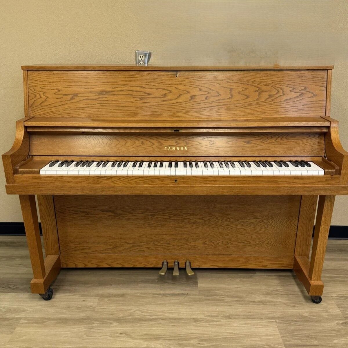 Yamaha upright piano with oak finish, featuring 88 keys and three pedals, ideal for aspiring pianists and studios.