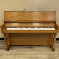 Yamaha upright piano with oak finish, featuring 88 keys and three pedals, ideal for aspiring pianists and studios.