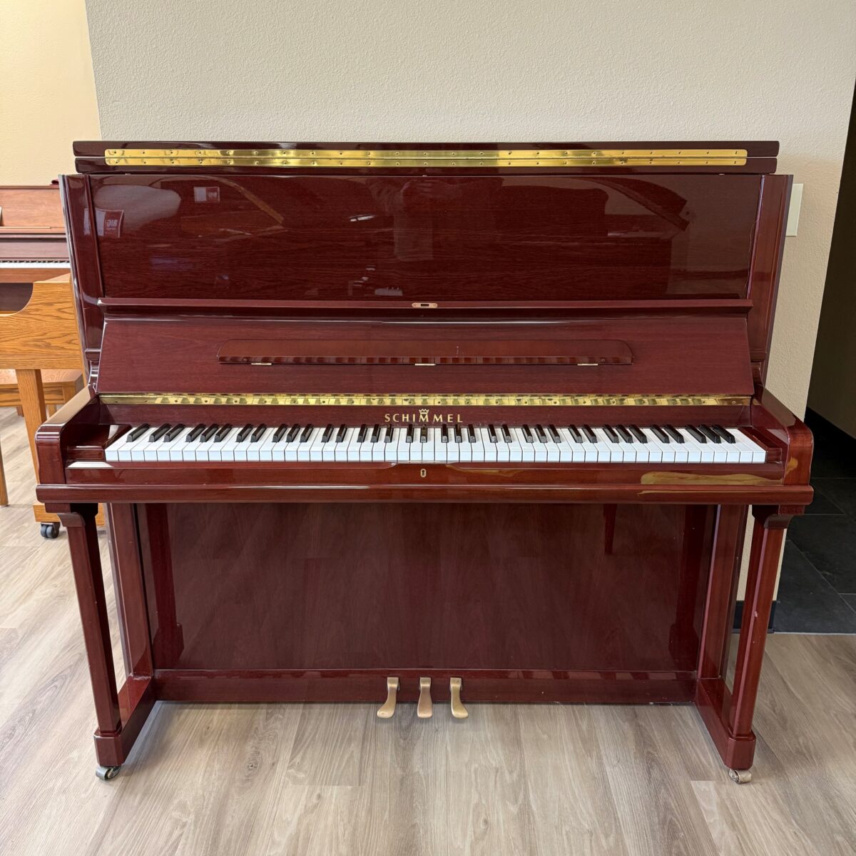 Schimmel upright piano in polished mahogany finish, featuring delicate keys and elegant brass accents, perfect for any musician.