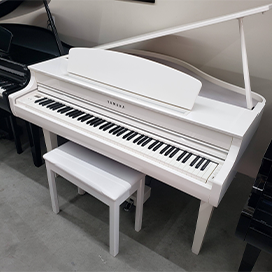 White Yamaha baby grand piano with matching bench in a showroom setting.